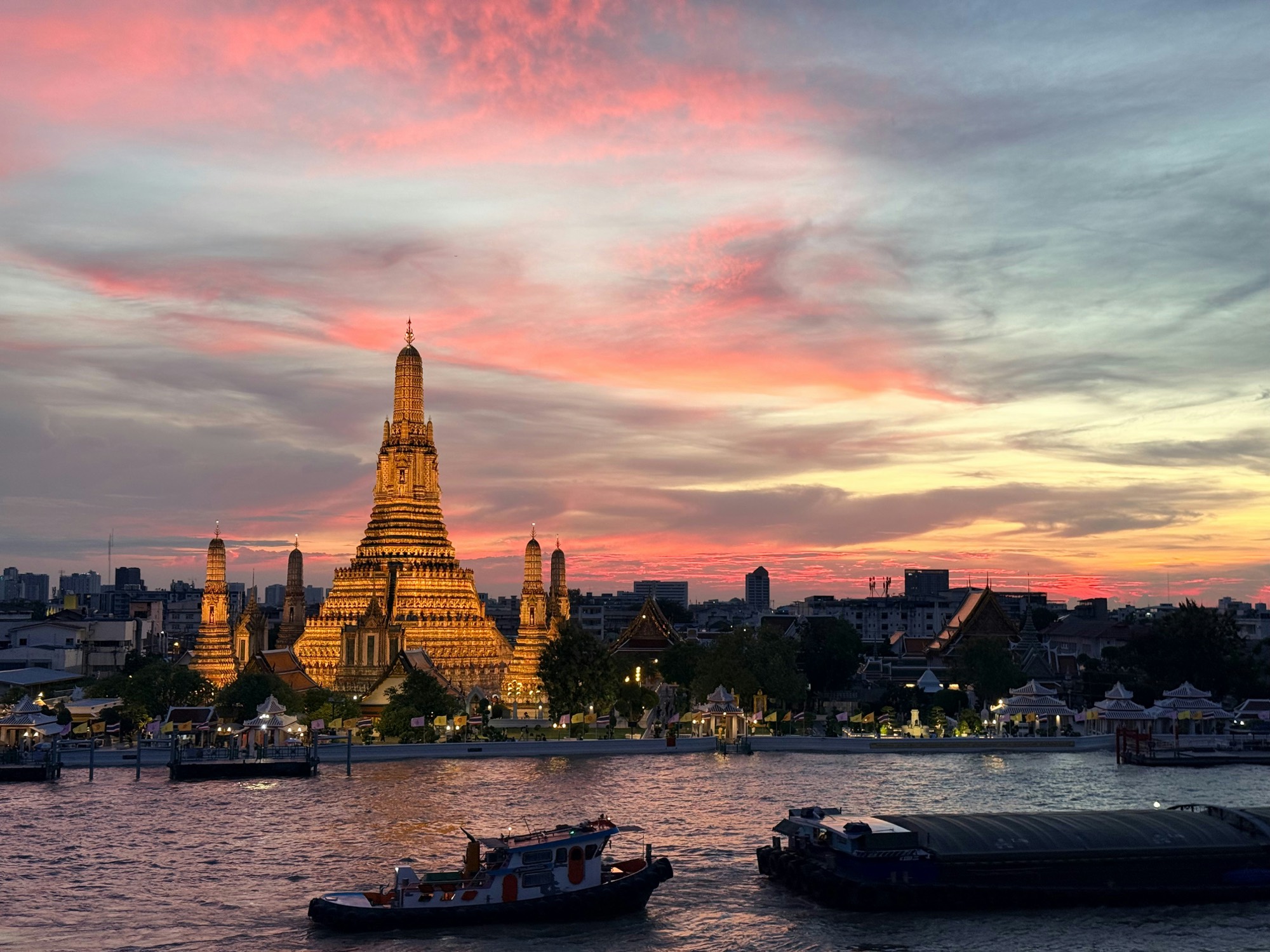 Wat Arun temple illuminated at sunset over the Chao Phraya River, Bangkok