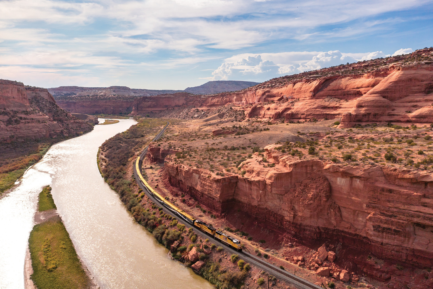 Aerial view of the Canyon Spirit train following the Colorado River through Ruby Canyon's red sandstone walls on the Rockies to the Red Rocks route.