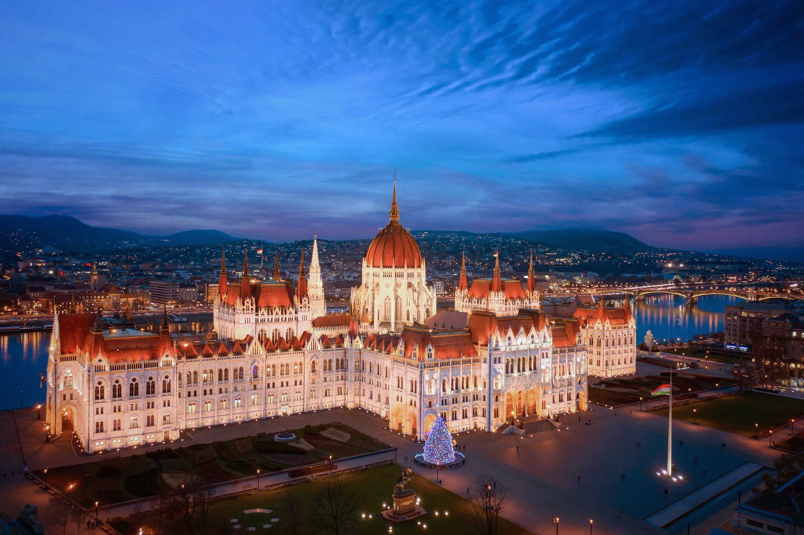 The Hungarian Parliament lit at dusk above the Danube, with a Christmas tree glowing on the Budapest embankment.