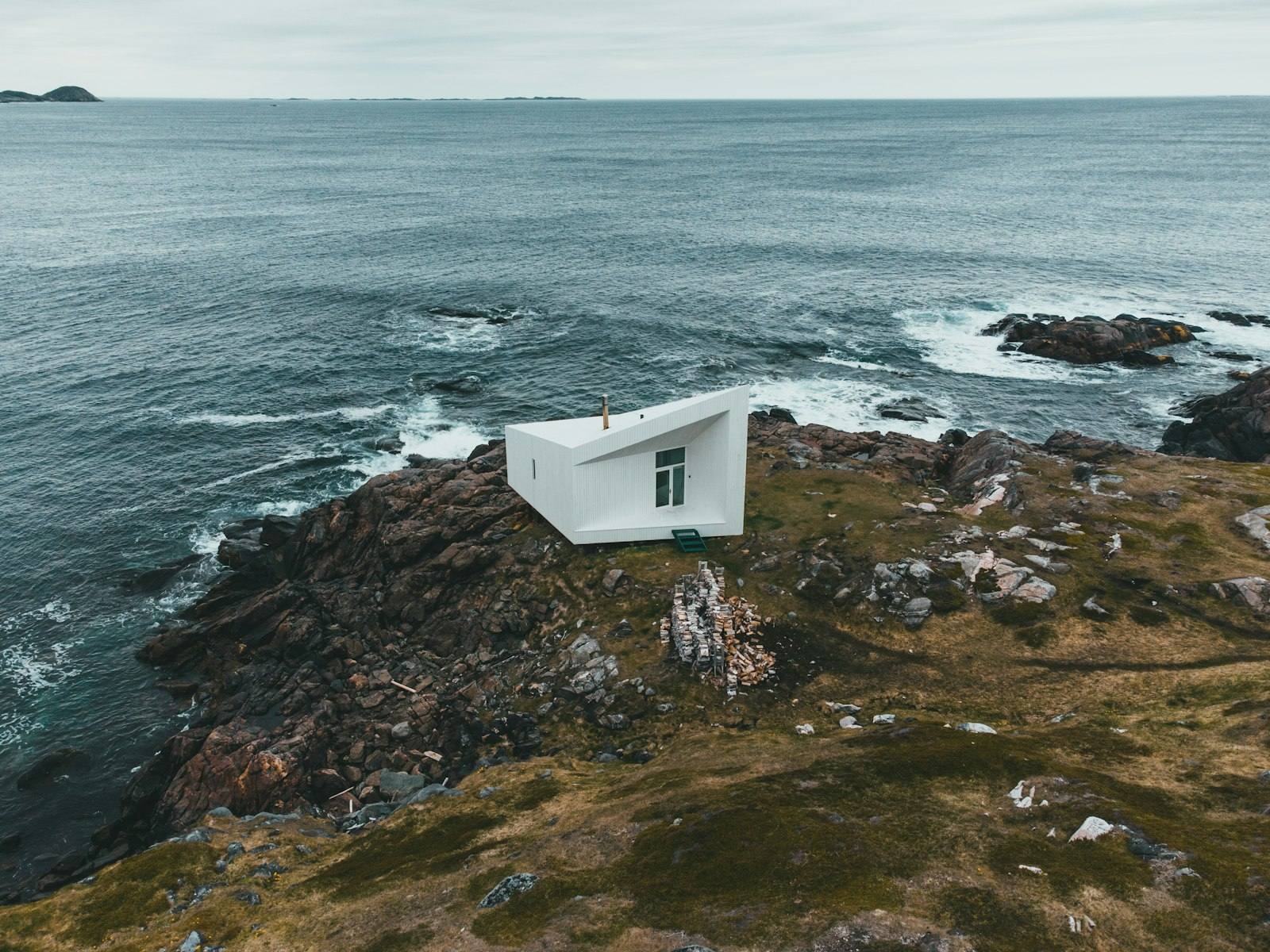 A single white artist's studio standing alone on bare rock on Fogo Island, the North Atlantic behind it.