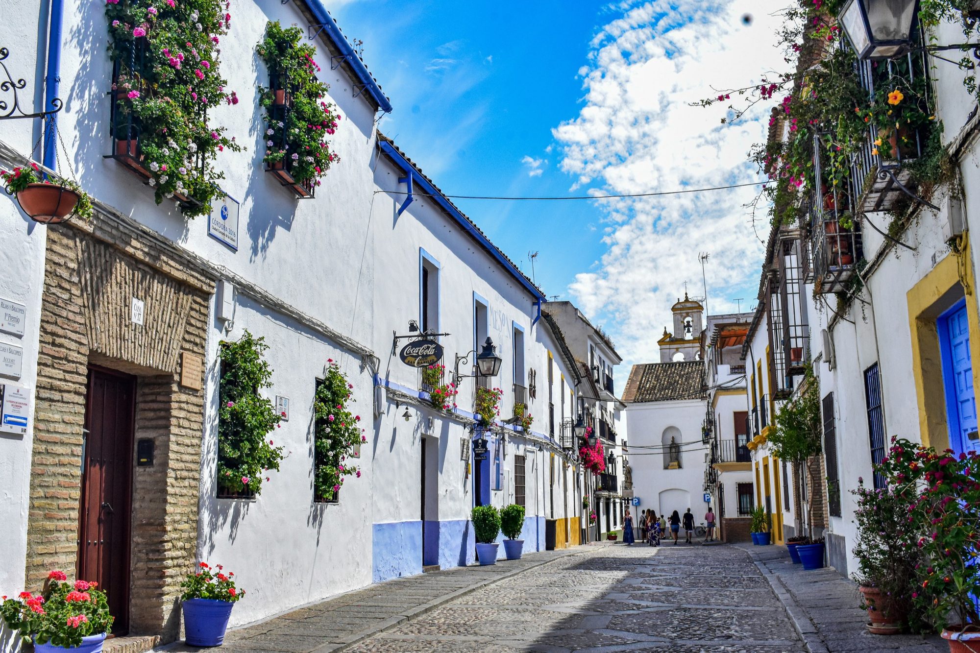 A narrow, whitewashed lane in Córdoba's old Jewish quarter, lined with flowerpots and worn cobblestones.