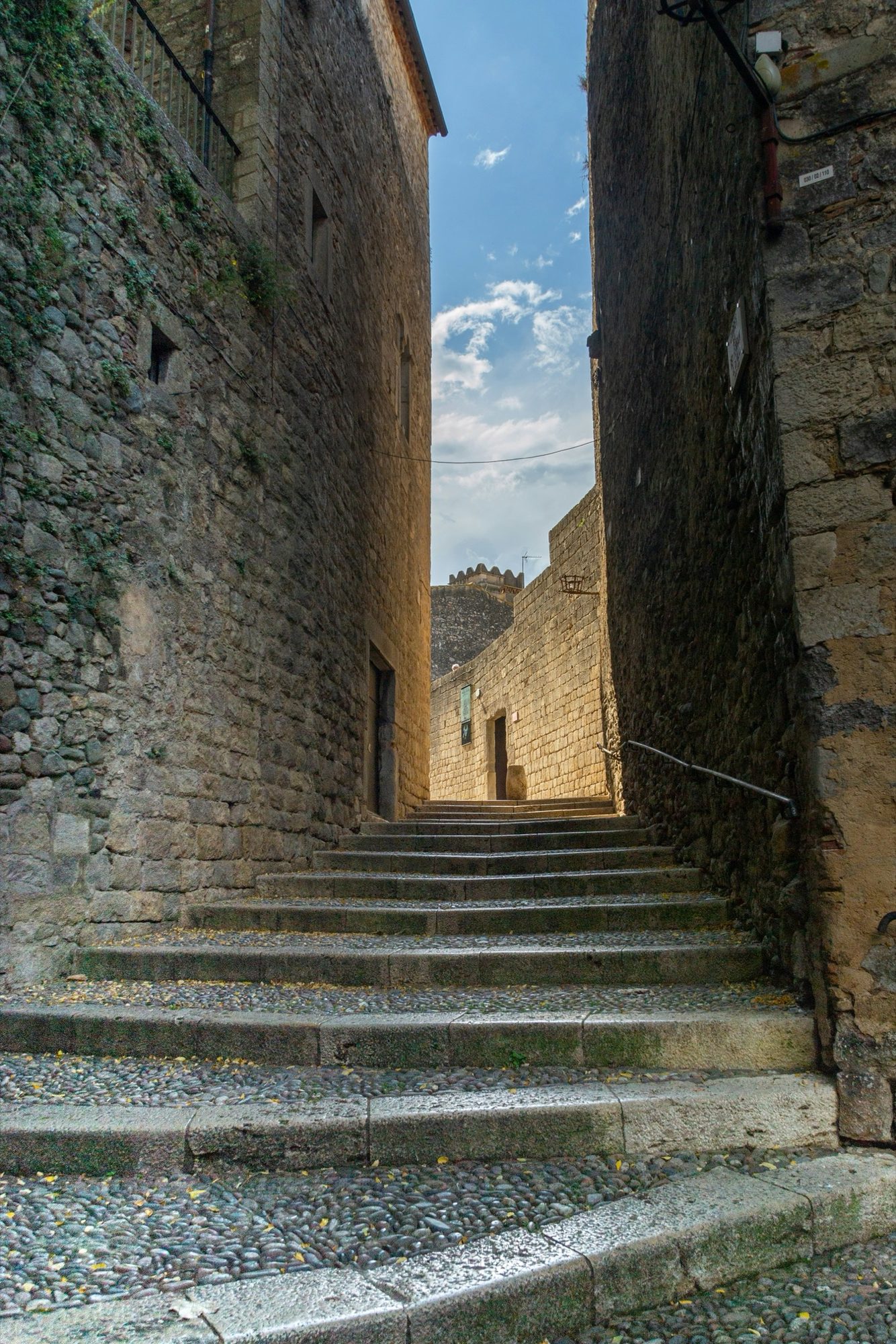 Worn stone steps climbing between tall medieval stone buildings in Girona's Call.
