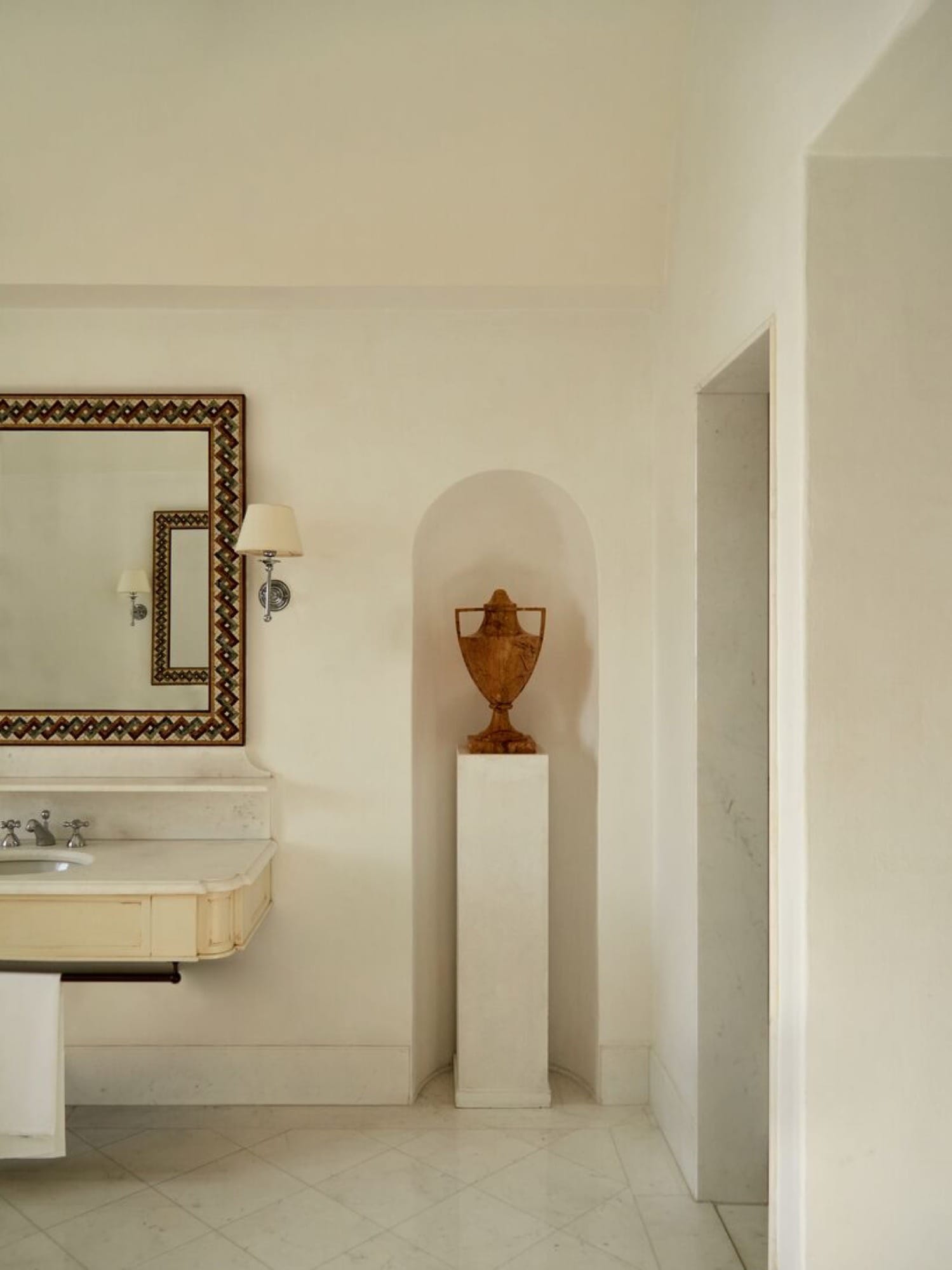 A Caruso suite bathroom — vaulted ceiling, marble vanity, mosaic-framed mirror, an antique urn in an arched alcove.