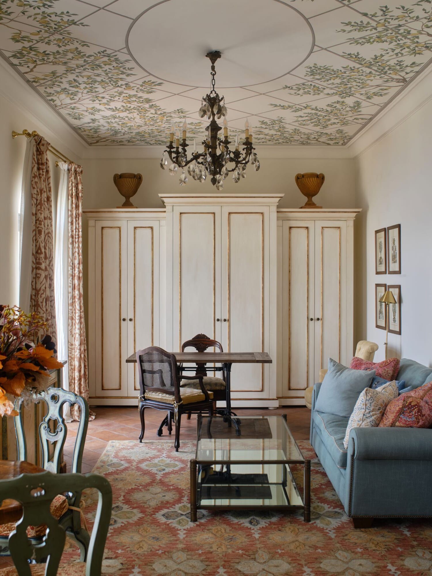 A palazzo suite sitting room — painted-foliage ceiling, cream wardrobes, period chairs around a desk, terracotta tile underfoot.