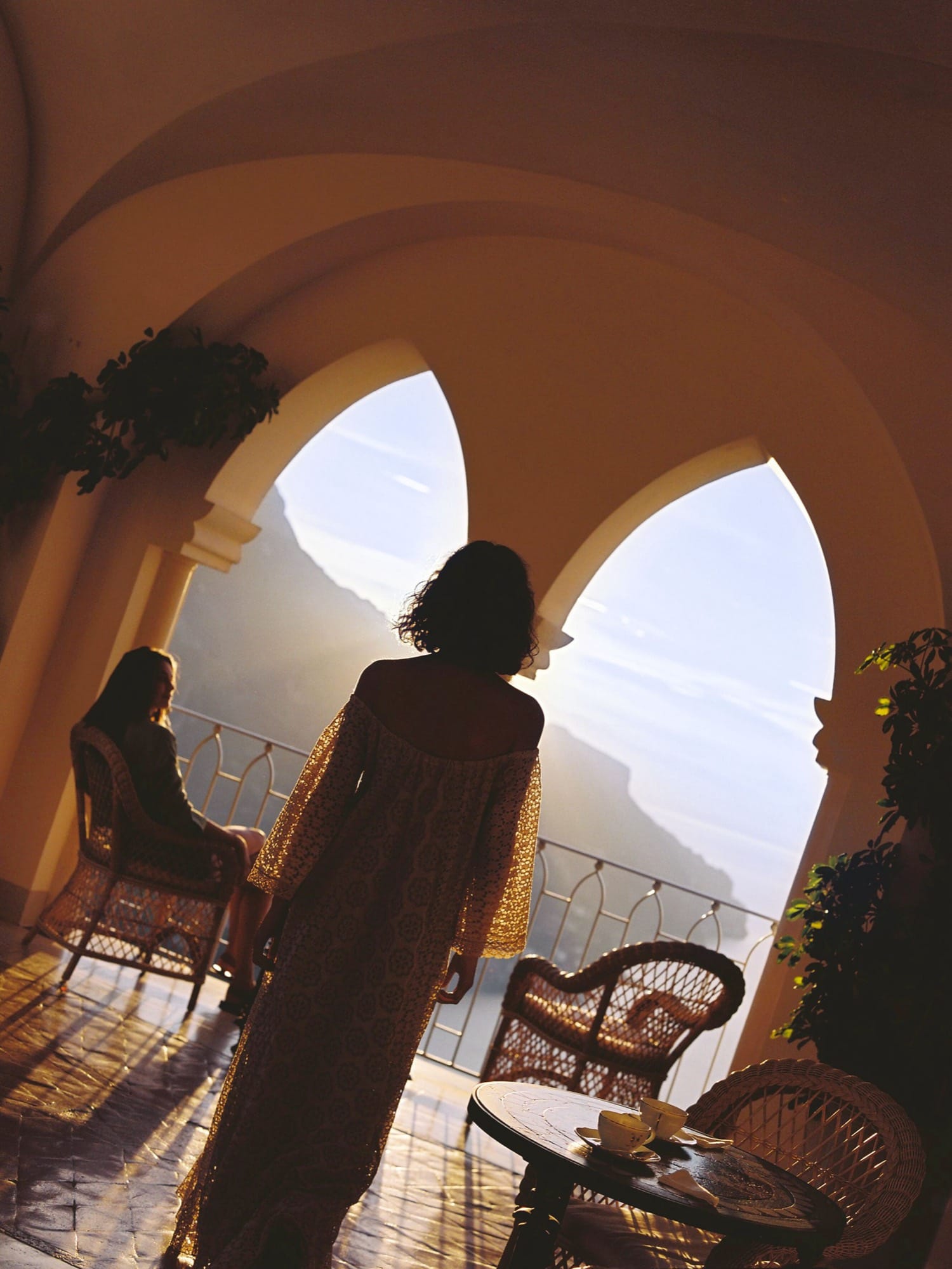 Two figures silhouetted in the Caruso's Moorish-arch terrace at dusk, looking out over the Amalfi Coast.