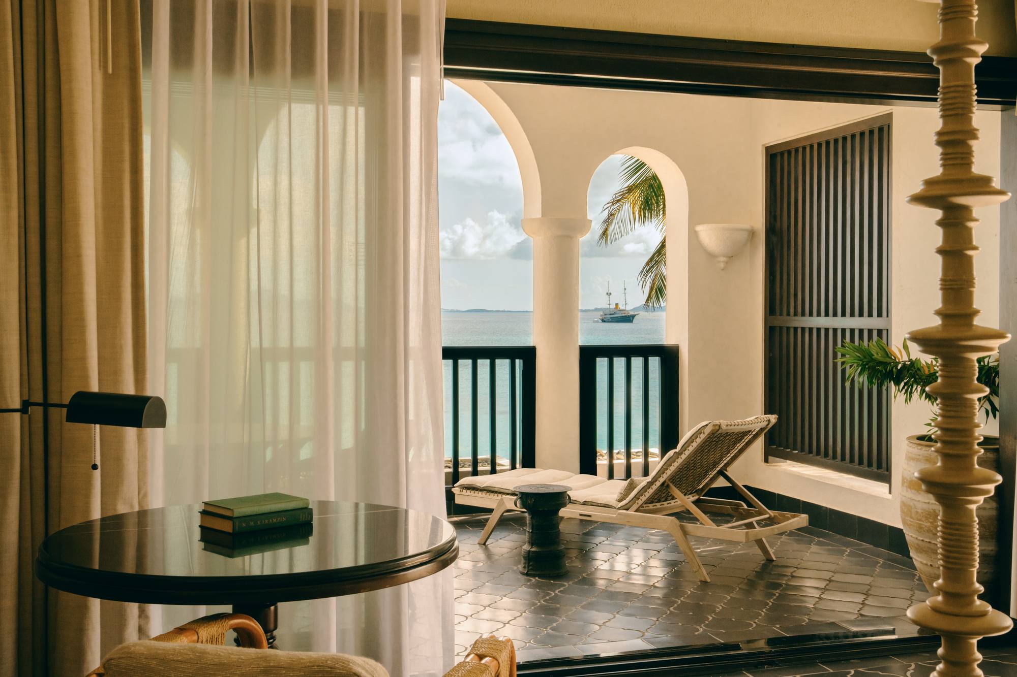 A light-filled suite interior at Cap Juluca, with a daybed on the terrace and palms beyond the arched doorway.