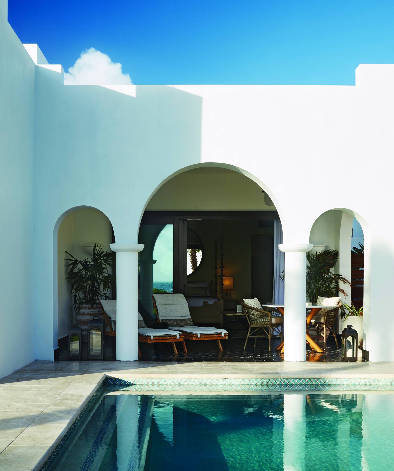 A Cap Juluca villa exterior — white Greco-Moorish arches, a private plunge pool, and loungers in the shade of the colonnade.
