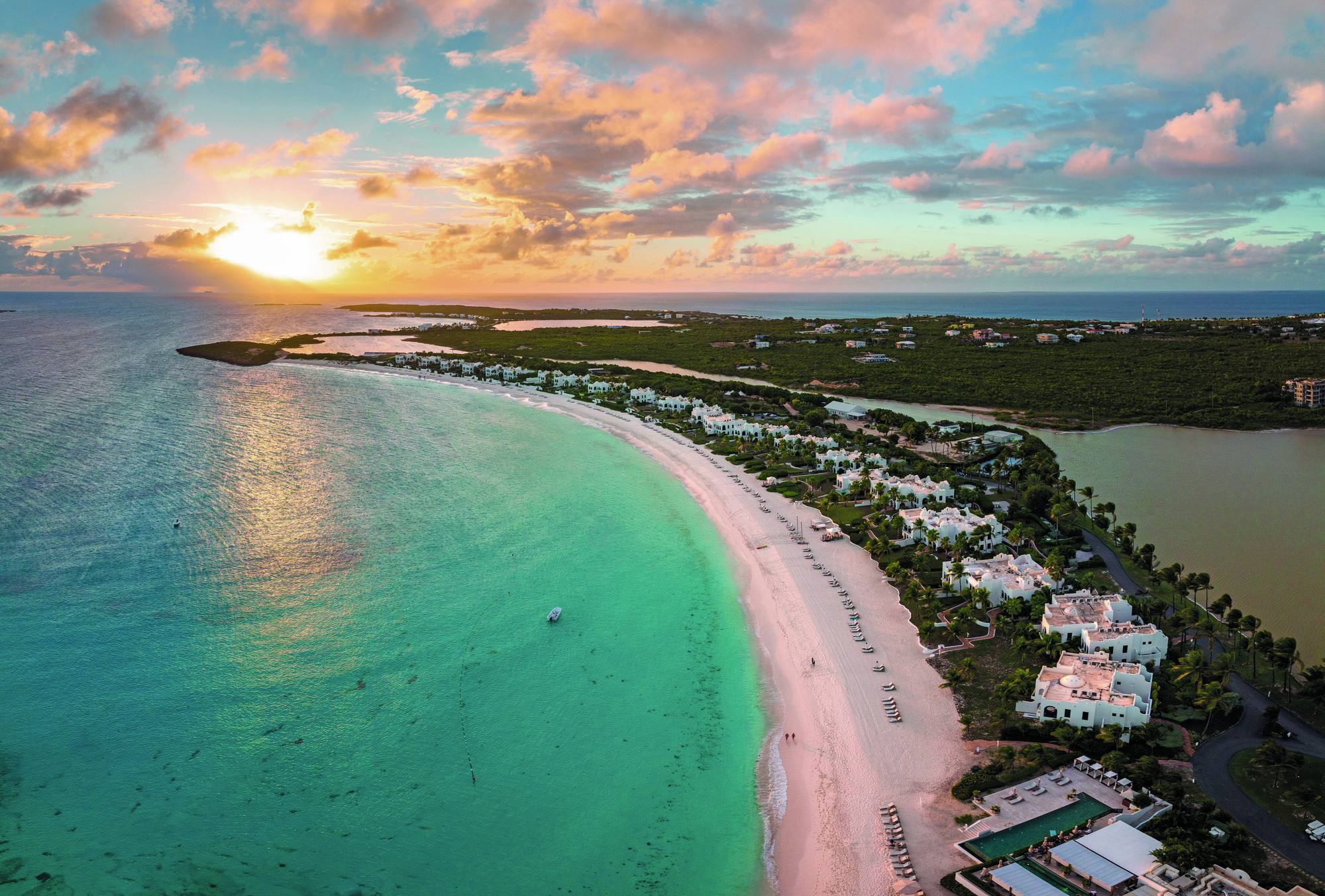 Aerial view of the curving Maundays Bay beach at sunset, a pink sky over turquoise water.