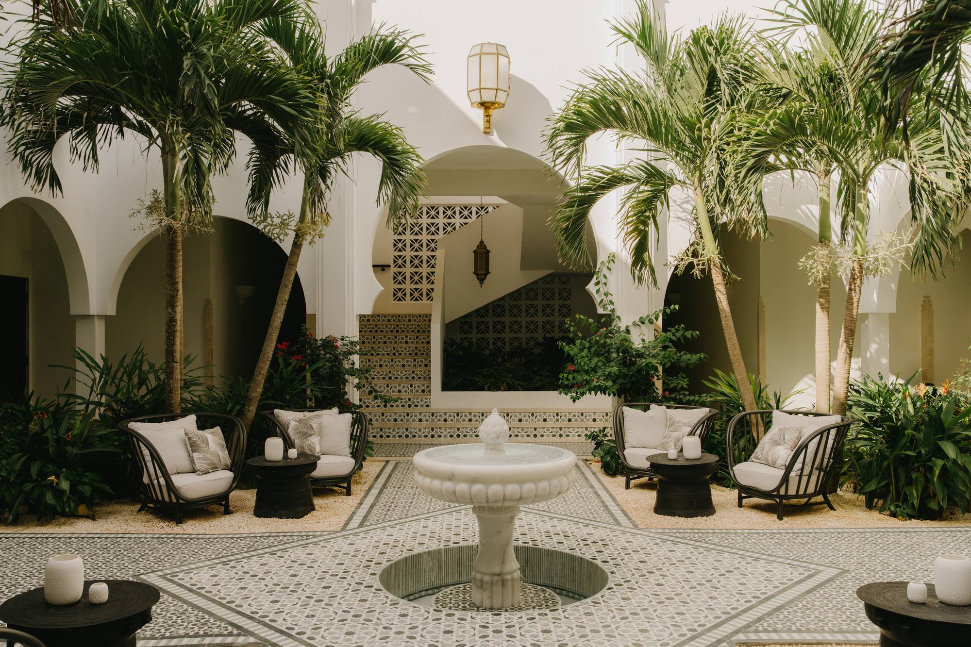 A Greco-Moorish courtyard at the Cap Juluca Spa by Guerlain, with tall palms, a round central table, and woven seating on patterned tile.
