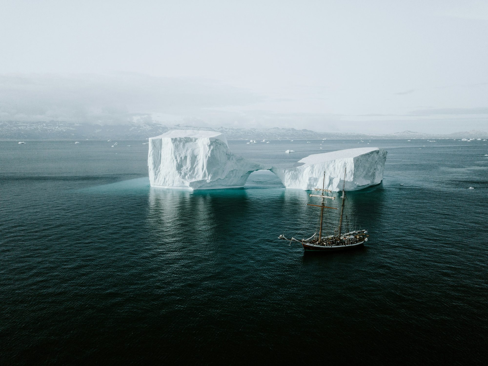 A small expedition ship dwarfed by icebergs and snow peaks along the Antarctic Peninsula