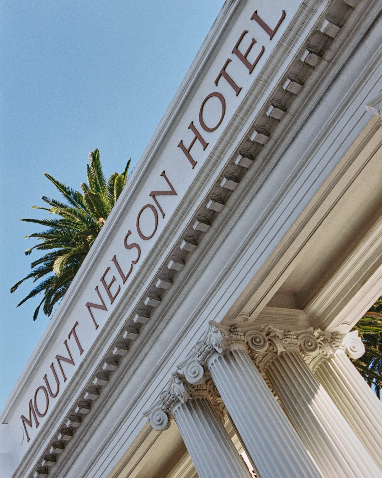 The Mount Nelson Hotel name carved above white Corinthian columns, palms behind