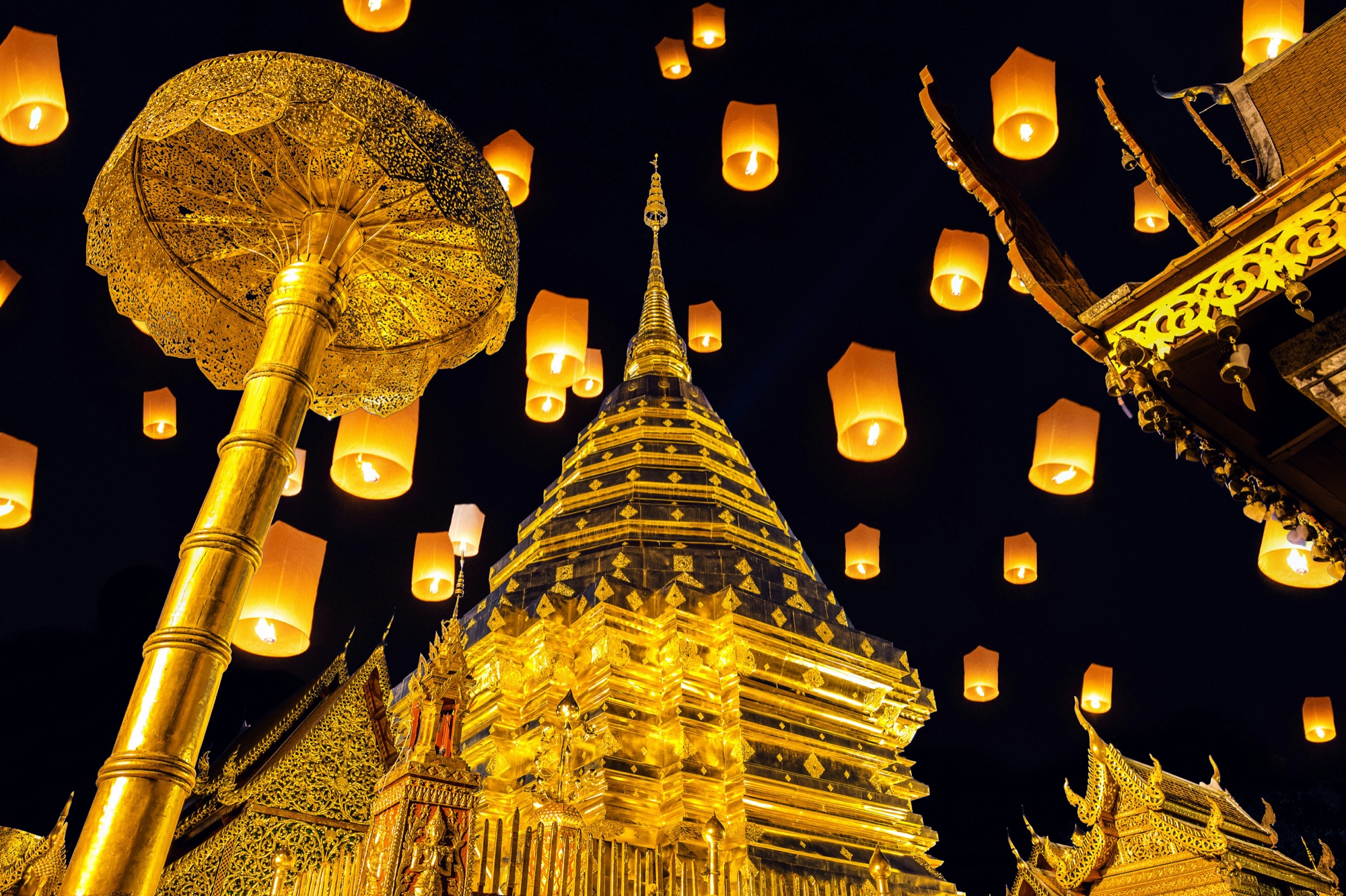 Glowing sky lanterns rising over the golden chedi of Wat Phra That Doi Suthep during the Yi Peng festival in Chiang Mai, Thailand
