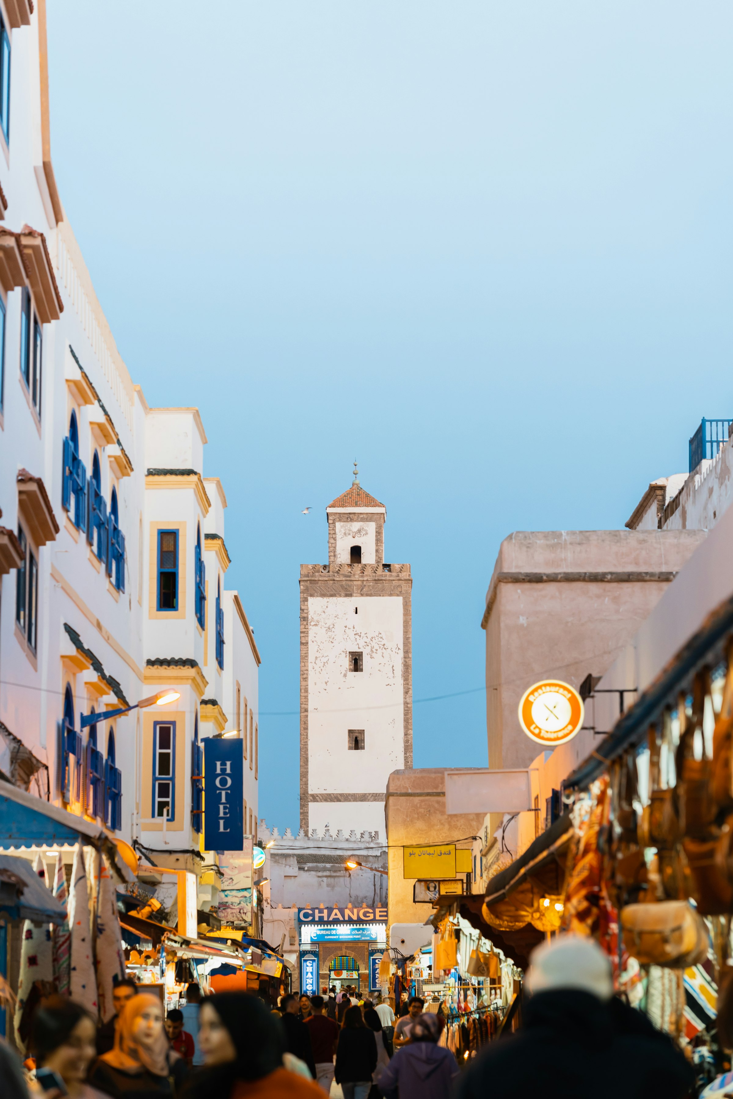 Essaouira's medina — whitewashed houses with blue shutters beneath a stone tower against a clear Atlantic sky.