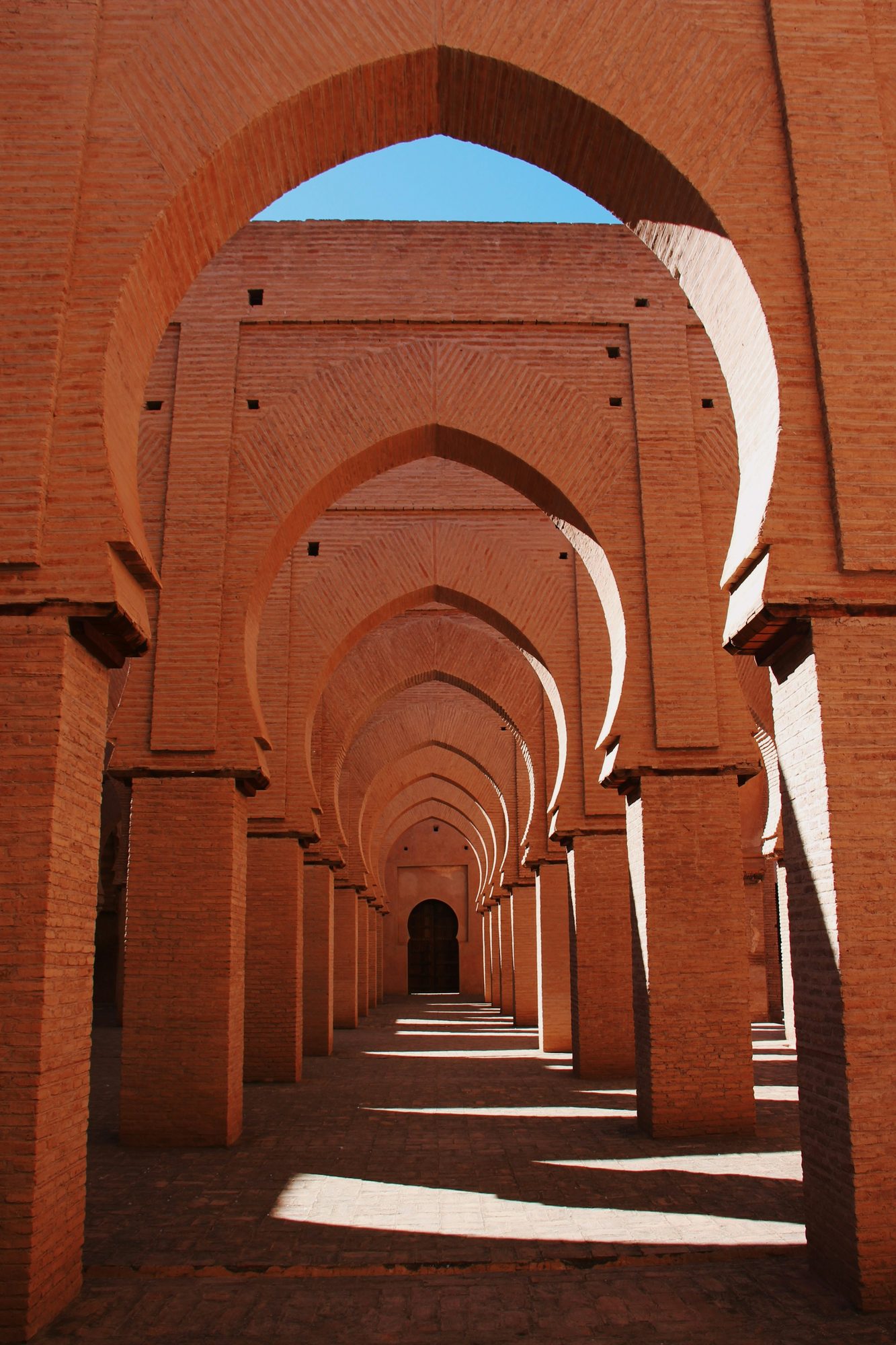 Sunlit corridor of terracotta Almohad brick arches, southern Morocco.