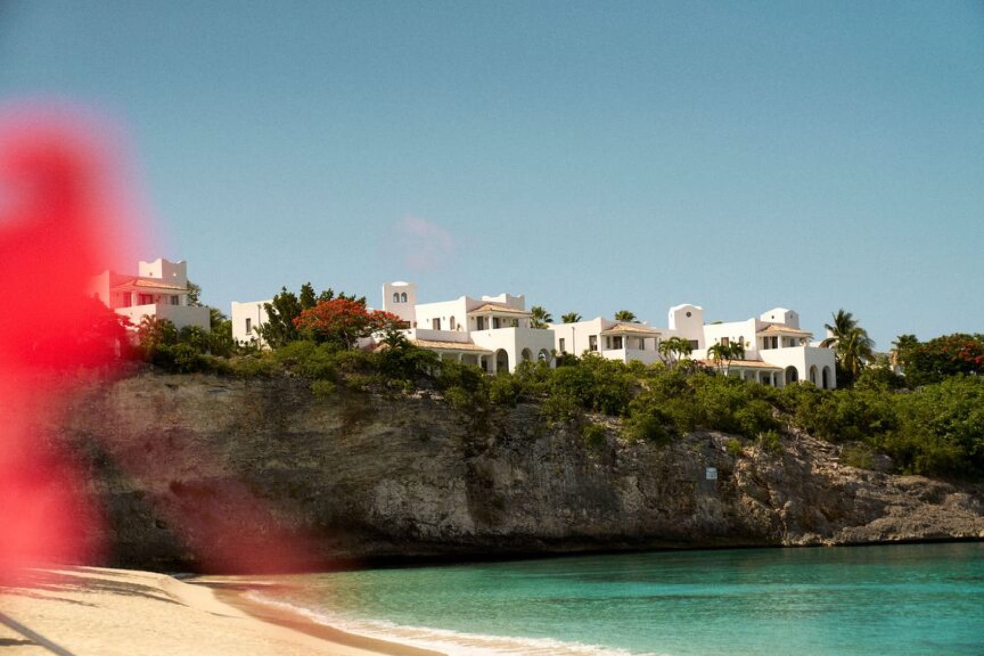 The architecture of La Samanna spilling down the cliffside to the Baie Longue beach — white-stone Mediterranean villas, terracotta roofs, palms, the curve of the cove ahead.