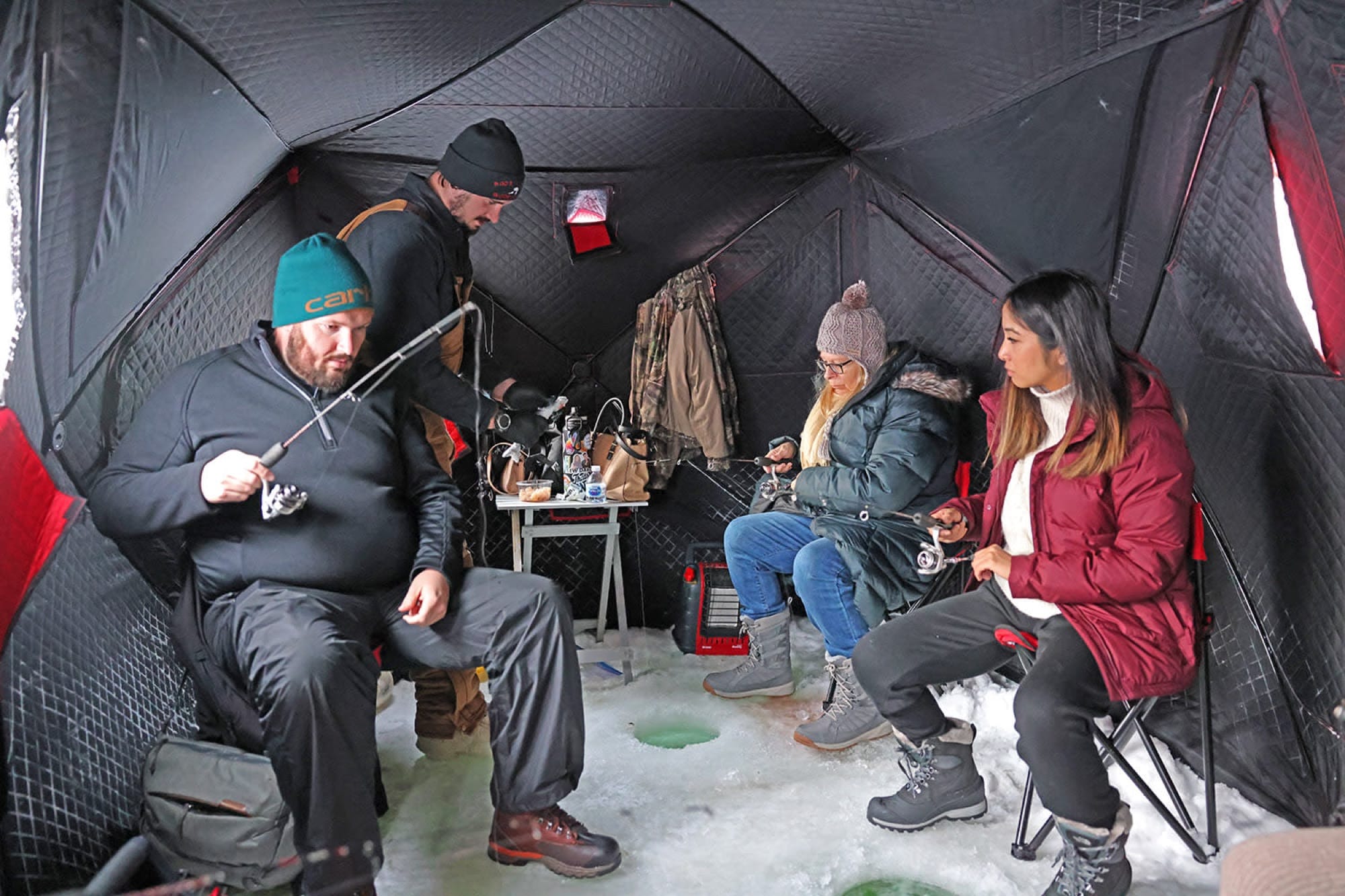 Travelers jigging lines through holes in the ice inside a heated fishing shelter.