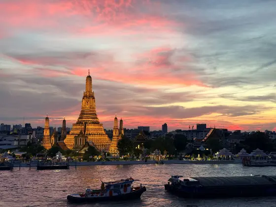 Wat Arun temple illuminated at sunset over the Chao Phraya River, Bangkok
