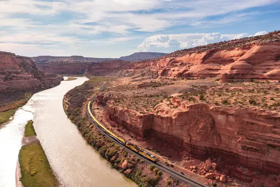 Aerial view of the Canyon Spirit train following the Colorado River through Ruby Canyon's red sandstone walls on the Rockies to the Red Rocks route.