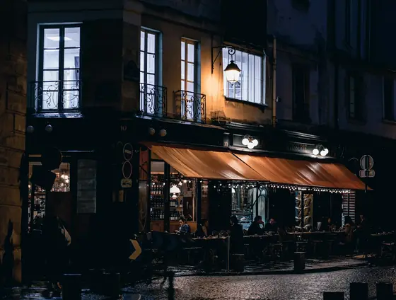 A corner café in Paris at night, its warm interior lit against a cold blue street.
