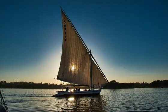 A felucca in silhouette on the Nile against a low sun, its sail lit from behind.