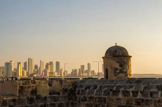 The ramparts of Cartagena's old city at dusk, a sentry box in silhouette and the modern skyline beyond.