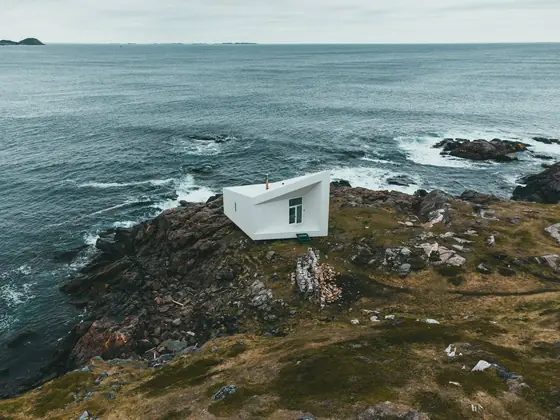 A single white artist's studio standing alone on bare rock on Fogo Island, the North Atlantic behind it.