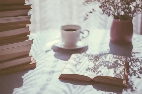 An open book resting beside a cup of tea on a table in soft morning light.