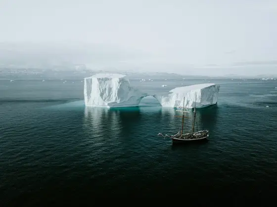A small expedition ship dwarfed by icebergs and snow peaks along the Antarctic Peninsula
