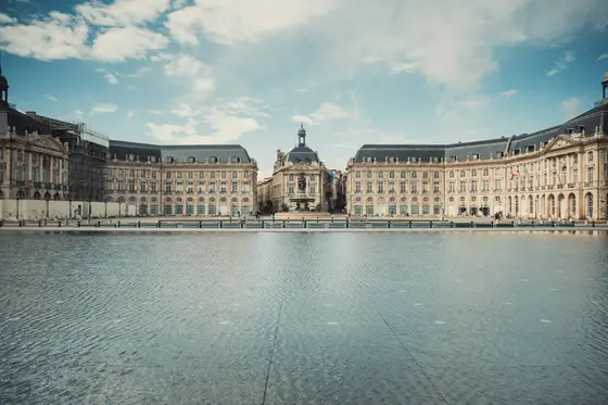 The curved 18th-century facade of the Place de la Bourse reflected in the Miroir d’eau in Bordeaux, France