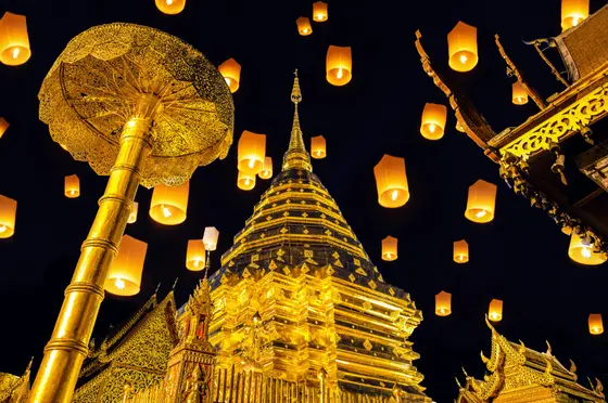 Glowing sky lanterns rising over the golden chedi of Wat Phra That Doi Suthep during the Yi Peng festival in Chiang Mai, Thailand