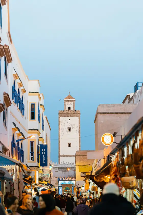 Essaouira's medina — whitewashed houses with blue shutters beneath a stone tower against a clear Atlantic sky.