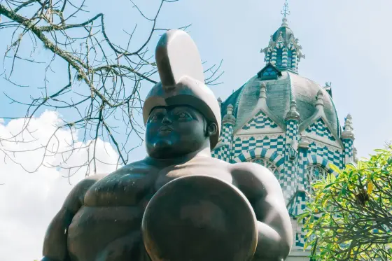 A Botero bronze sculpture in Plaza Botero with the checkerboard dome of the Palace of Culture behind, in Medellin, Colombia