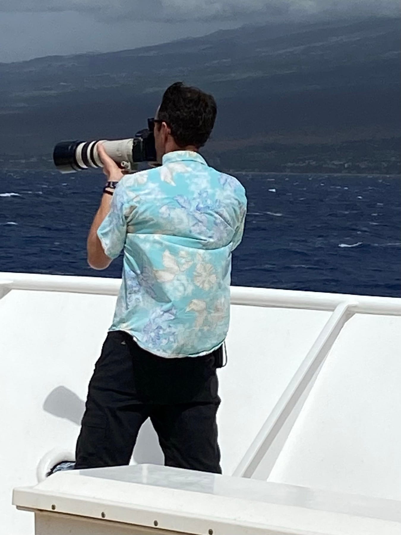 A photographer on the deck of Safari Explorer in Hawaii, lens trained on humpback whales — the small-ship Hawaiian experience.