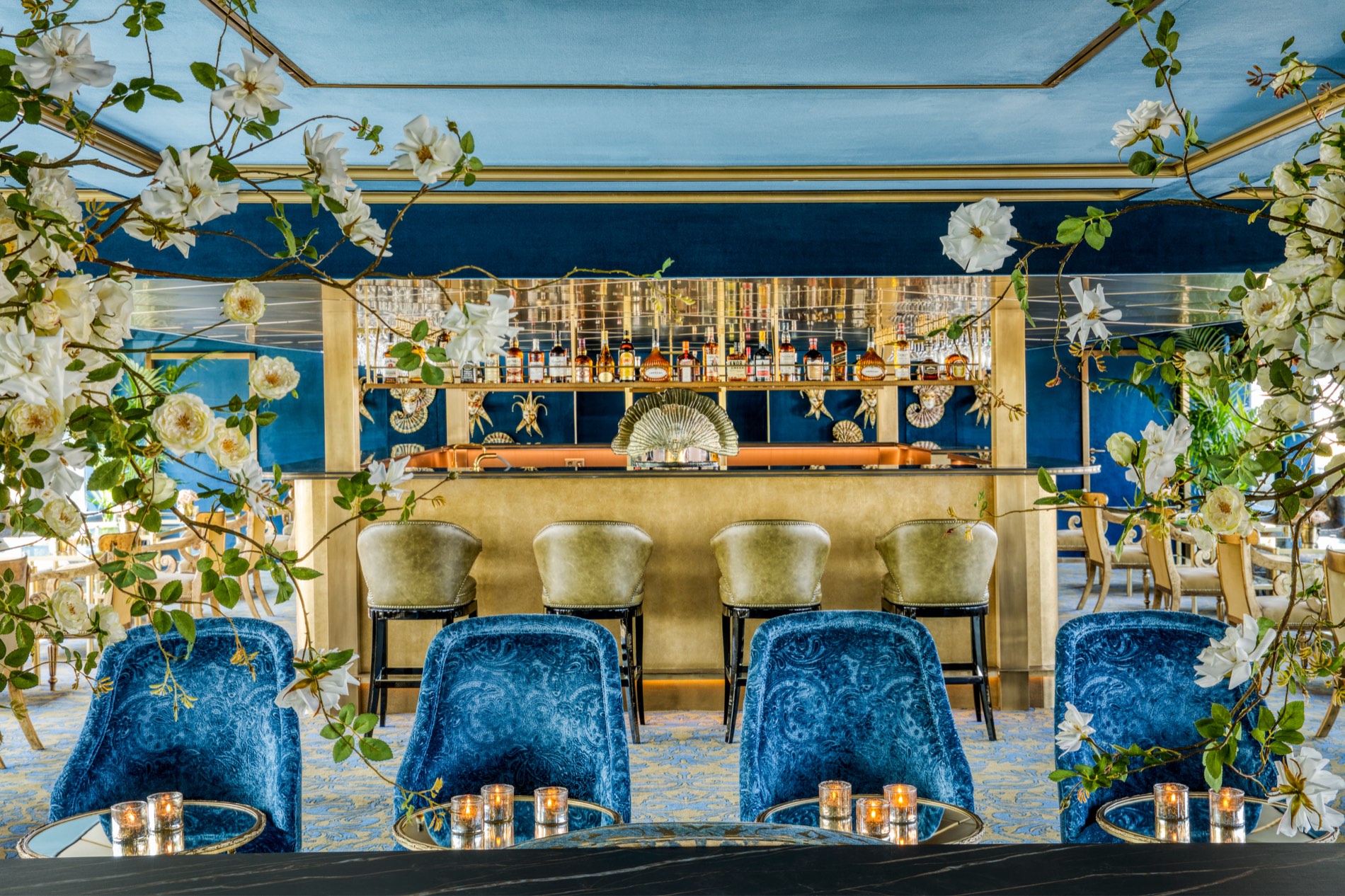 The S.S. La Venezia lounge — blue-velvet paisley chairs, a gilded bar, white roses, and Venetian carnival masks on a deep-blue wall.