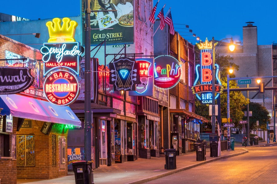 Beale Street in Memphis at dusk, neon signs for the blues clubs and the Music Hall of Fame stacked along the brick storefronts.
