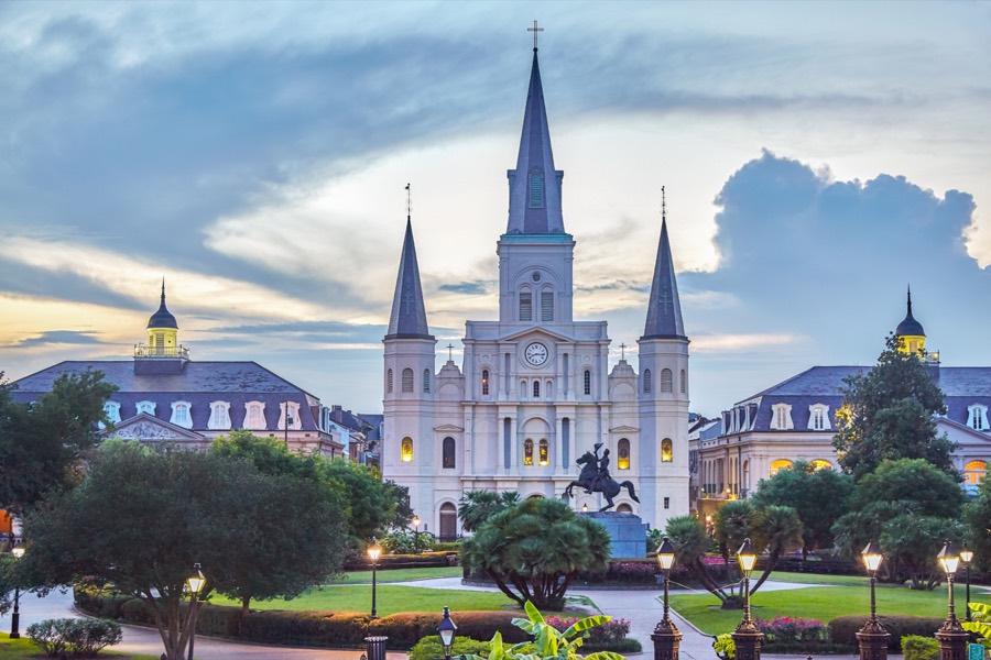 Jackson Square at dusk, the three spires of St. Louis Cathedral above the palms and street lamps of the French Quarter.