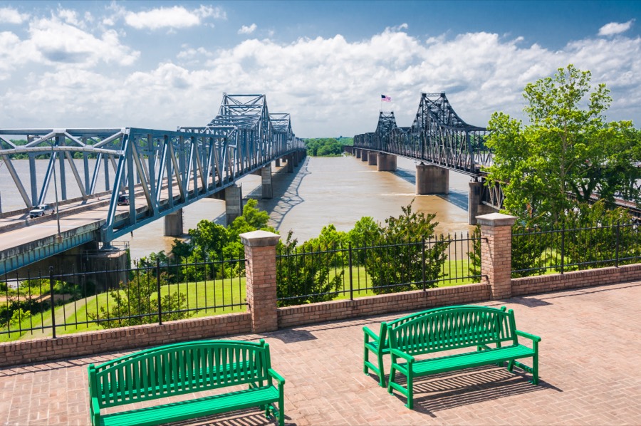 The two Mississippi River bridges at Vicksburg seen from a riverfront walk lined with green benches.