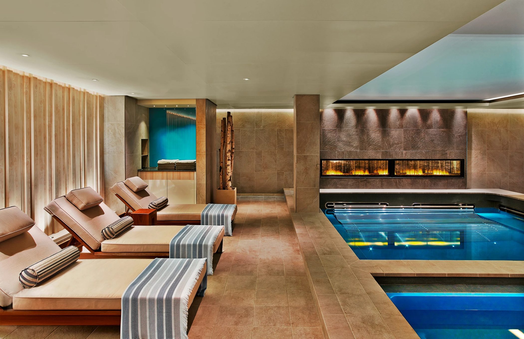 The Nordic Spa on a Viking ocean ship — teak loungers with striped throws along a stone wall on the left, a lit thermal pool and a long horizontal fireplace on the right.