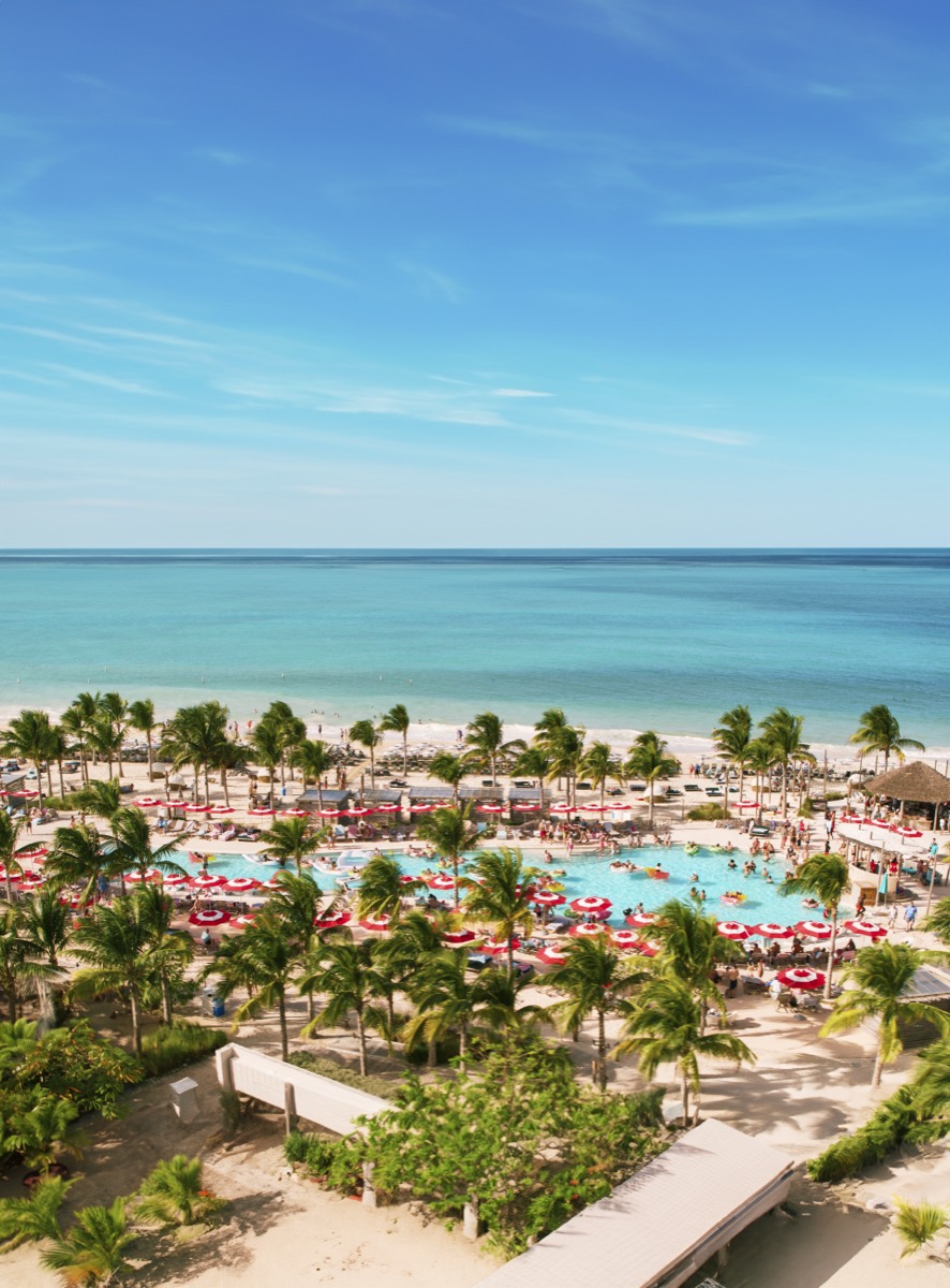 Aerial view of the Beach Club at Bimini — turquoise water, palm trees, and red umbrellas ringing the pool.