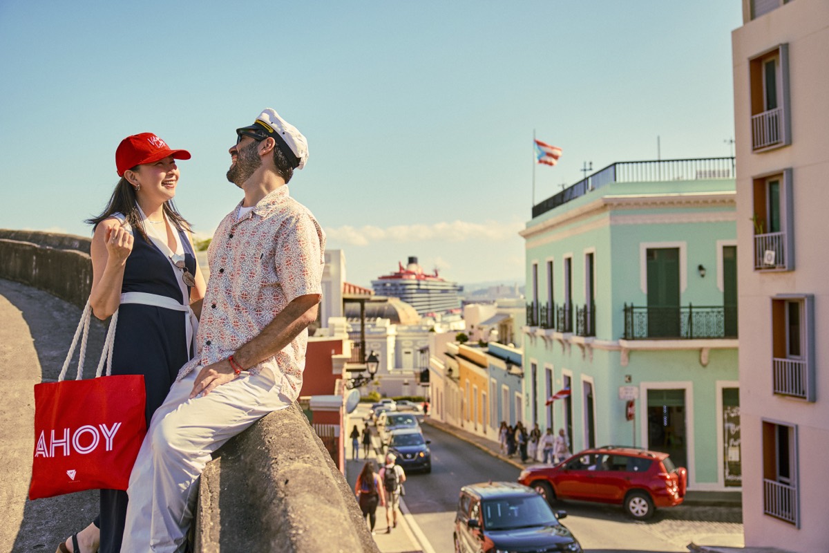 A couple on the old city walls of Old San Juan, a Virgin Voyages ship in the harbor below.