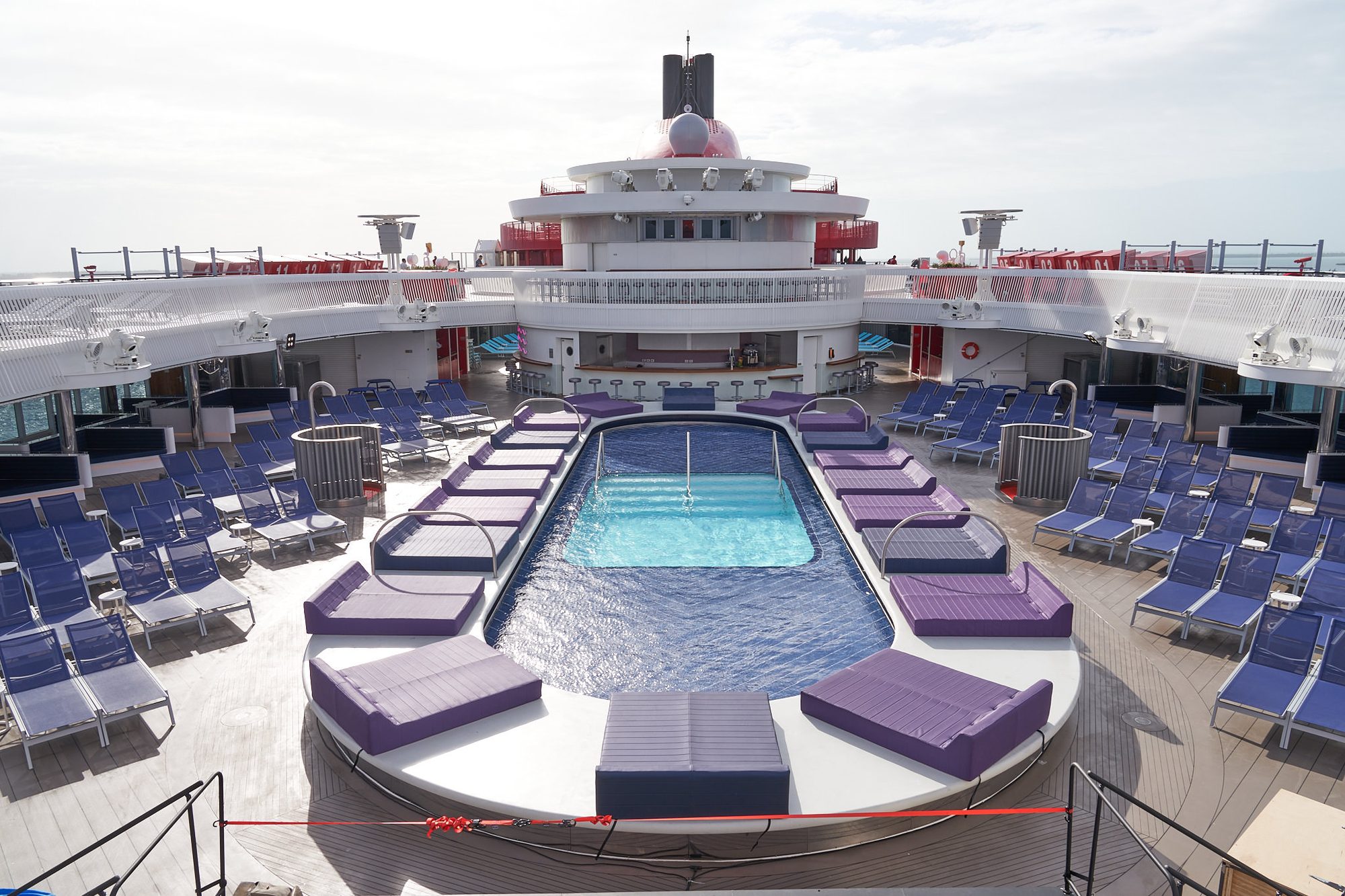 The Aquatic Club pool deck aboard a Virgin Voyages ship — adults in the pool, loungers under the sun.