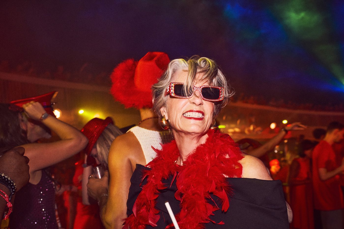 Scarlet Night — a sailor in red feathers and sunglasses laughing on the pool deck, the ship lit red behind her.