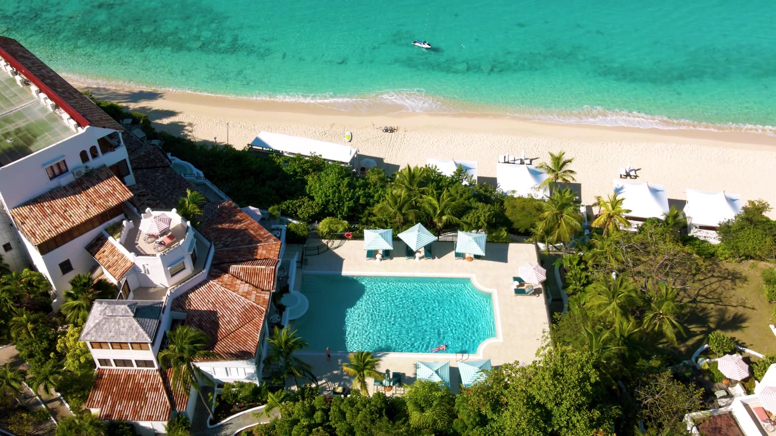 Aerial view of La Samanna's main pool, beach umbrellas in tents along the sand, the cove curving to the headland.